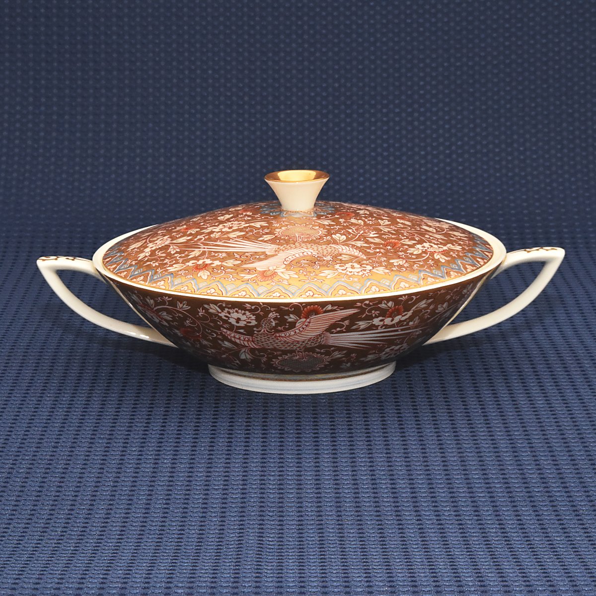 明治初期にデザインされた金襴手鳳凰紋のデザインをモチーフにしたデザインです。繊細で巧妙に描かれた鳳凰と唐草文の周囲を金襴手で埋め尽くし縁を地紋で埋めた豪華絢爛な絵付けです。ワンランク上のティータイムを味わえるオススメのキャセロールです。
サイズ:胴径23*高11㎝です。